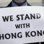 Man holding sign saying We Stand With Hong Kong
